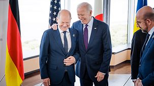 US-Präsident Biden legt die Hand auf die Schulter von Bundeskanzler Scholz, beide lächeln.