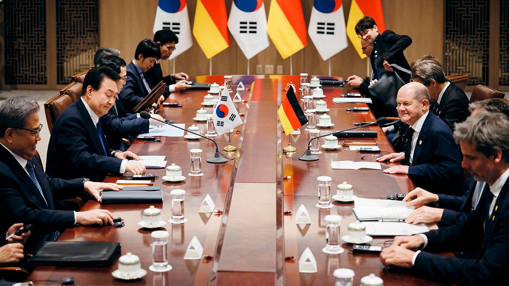 Federal Chancellor Scholz and the President of the Republic of Korea, Yoon Suk-yeol, and their respective delegations facing one another at a large table.