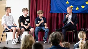 Bundeskanzler Scholz im Gespräch mit drei Schülern auf Podium