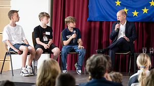 Bundeskanzler Olaf Scholz im Gespräch mit Schülern beim Besuch einer Schule im Rahmen des EU-Projekttages an Schulen.