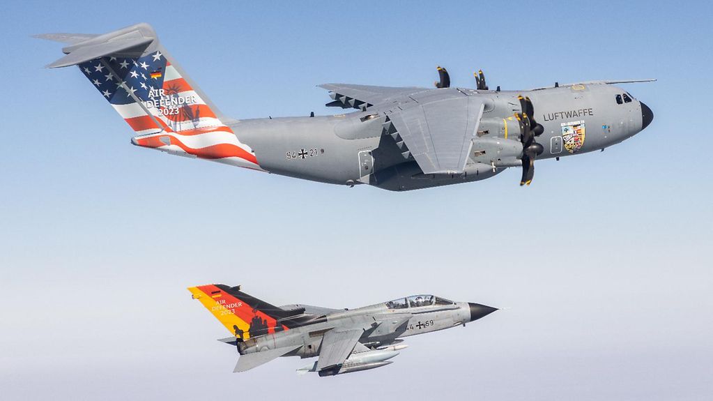 Un avion de transport de type Airbus A400M et un avion de combat Tornado de l’armée de l’air allemande portant sur les empennages le drapeau allemand et le drapeau américain volent côte à côte.