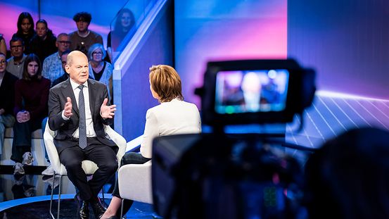 Bundeskanzler Olaf Scholz zusammen mit Sandra Maischberger im Fernsehstudio. Im Vordergrund eine Kamera.