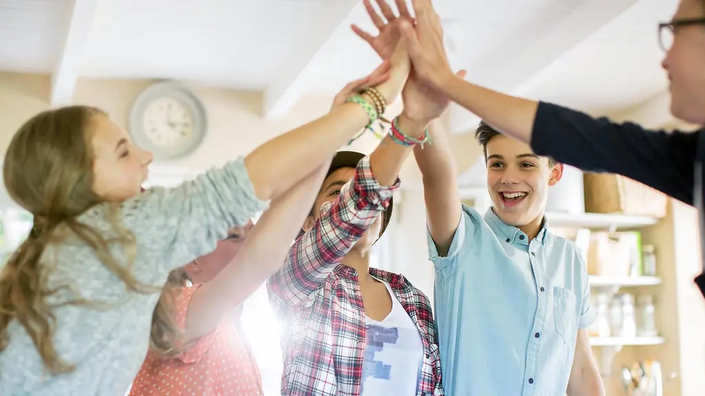 Gruppe von Teenagern macht High Five im Wohnzimmer