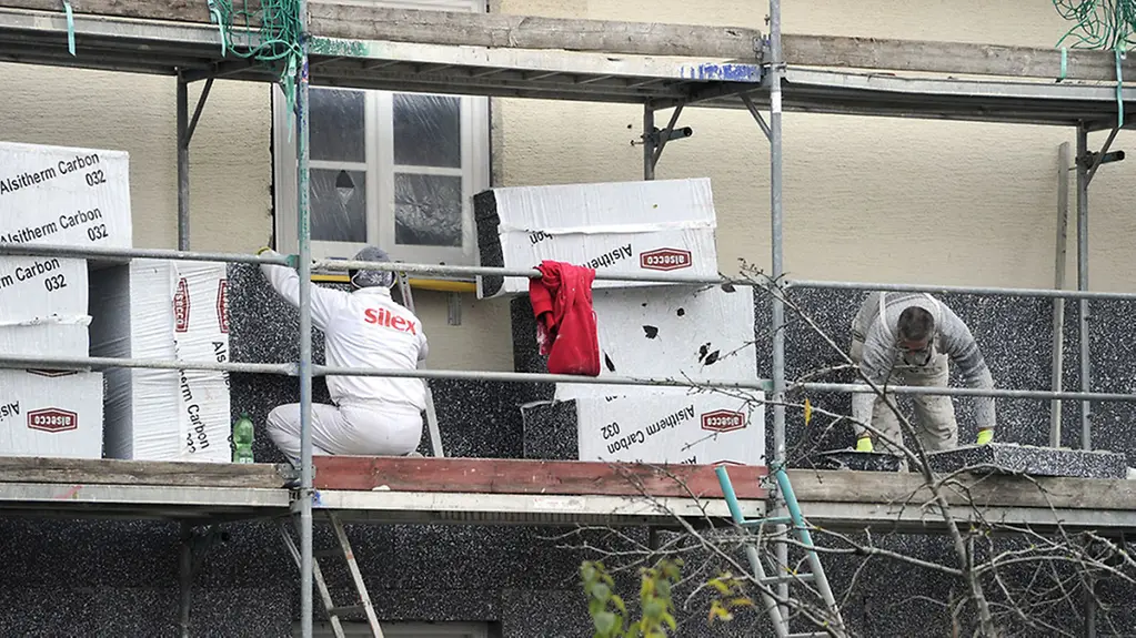 Fassadendämmung an einem Altbau - Arbeiter dämmt eine Hausfassade.