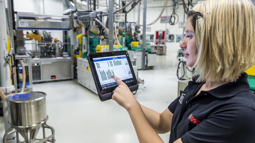 Eine Mitarbeiterin prüft mit einem Tablet die Betriebsdaten von vernetzten Maschinen