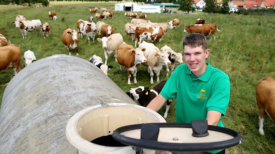 Ein Auszubildender öffnet einen Wassertank auf einer Weide mit Rinderherde