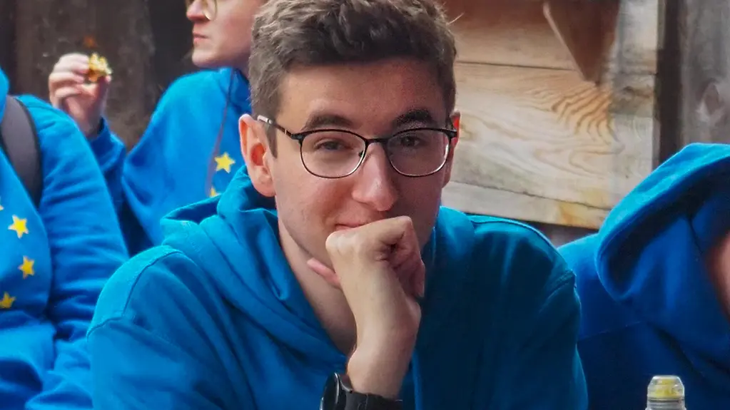 Ein junger Mann im Vordergrund mit blauem Pullover.