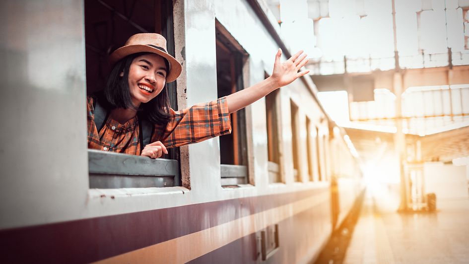 Jugendliche winkt aus einem Zug-FensterSmiling Young Woman In Train