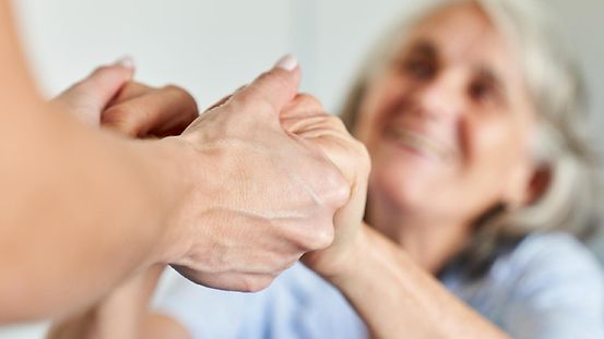 Eine Person hält fürsorglich die Hände einer Seniorin.