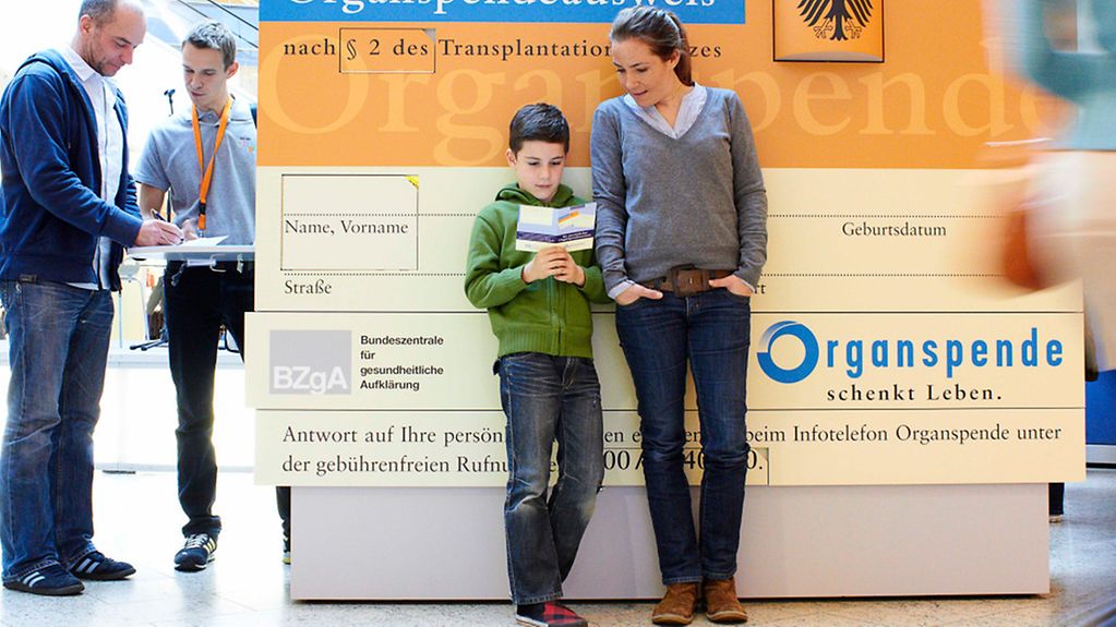 Mutter und Kind vor einem Plakat mit Organspendeausweis