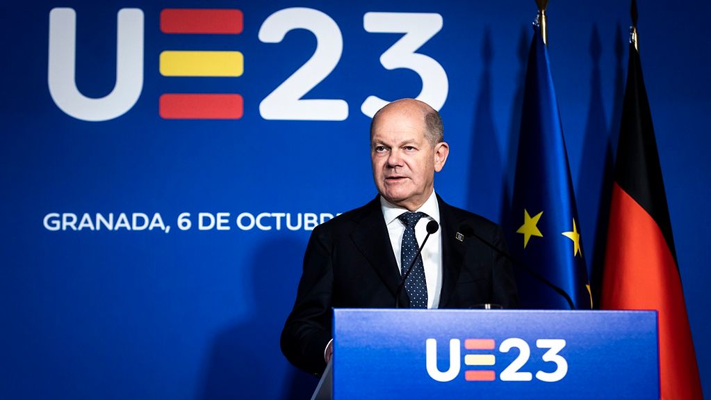 Bundeskanzler Olaf Scholz steht an einem Rednerpult mit Mikrofon. Neben ihm hängen die Flaggen von der EU und von Deutschland.