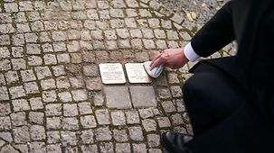 Le chancelier fédéral Olaf Scholz frottant les pavés de mémoire dédiés aux époux Goslar.