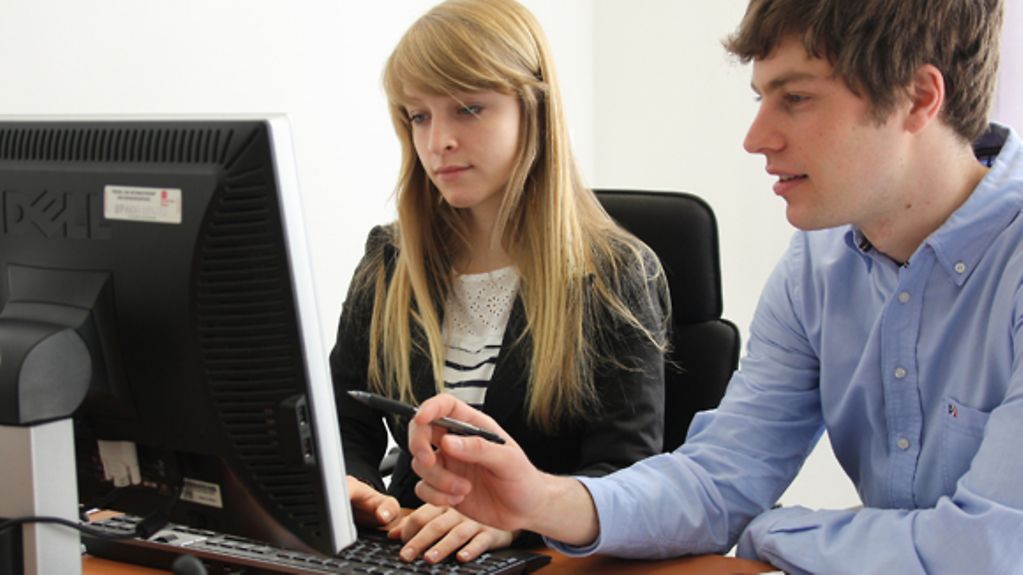 Zwei junge Praktikanten sitzen vor einem Bildschirm