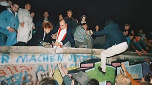Menschen klettern auf Westberliner Seite auf die Mauer.