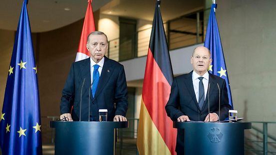 Bundeskanzler Olaf Scholz und der türkische Präsident Erdogan sprechen mit der Presse. Im Hintergrund sieht man die Flaggen von der Türkei und von Deutschland. Links und rechts daneben ist die Flagge von Europa.