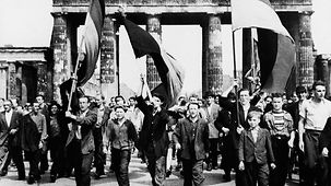 Demonstranten, vorwiegend junge Männer, gehen durch das Brandenburger Tor. Einige halten Deutschlandflaggen hoch. 
