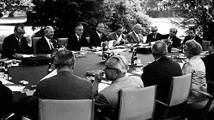 Das Bundeskabinett unter der Leitung von Kurt Georg Kiesinger tagt an einem großen Tisch im Park des Palais Schaumburg.