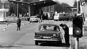 Mehrere Fahrzeuge und Polizisten an einem Berliner Grenzübergang. Ein Polizist beugt sich zu einem Fahrzeug mit Westberliner Kennzeichen herab.