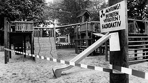 Ein leerer Kinderspielplatz, abgesperrt durch ein Plastikband. An einem Baum ist eine Schild angebracht mit der Aufschrift: Achtung! Betreten verboten! Radioaktiv.