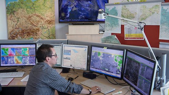 Ein Mitarbeiter sitzt vor fünf Bildschirmen, auf denen er verschiedene Wetterkarten und Messwerte beobachtet.