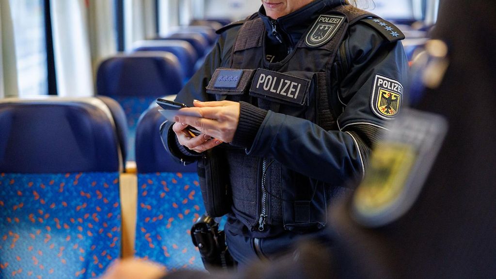 À bord d’un train, des policiers fédéraux contrôlent les papiers d’un passager entrant sur le territoire. (Pour plus d’informations, une description détaillée est disponible sous l’image.)