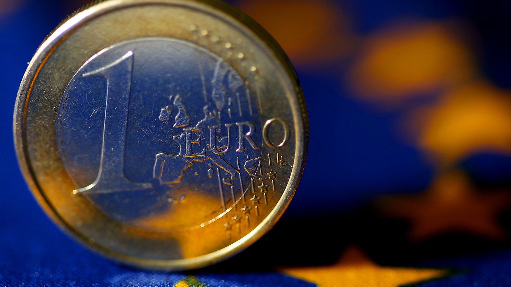 Eine Euromünze vor der Europa-Flagge.