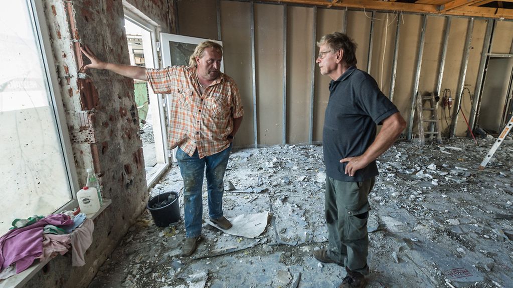 Zwei Männer sprechen in einem vom Hochwasser zerstörten Büro miteinander.