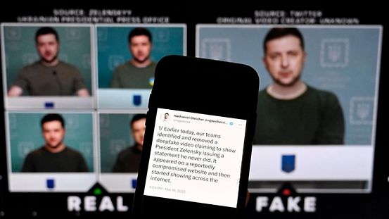 Das Bild zeigt einen Handybildschirm auf dem eine Erklärung des Leiters der Sicherheitspolitik bei META zu sehen ist. Im Hintergrund ein gefälschtes Video, in dem der ukrainische Präsident seine Soldaten auffordert, ihre Waffen niederzulegen. 