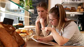 Eine Kaffeebesitzerin mit Donwsyndrom diskutiert mit einer Mitarbeiterin.