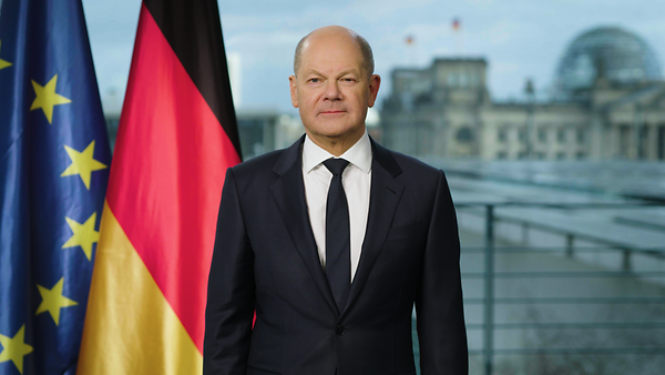 Bundeskanzler Scholz vor einem Bild des Deutschen Bundestages, neben ihm stehem die Flagge der Europäischen Union und die der Bundesrepublik Deutschland