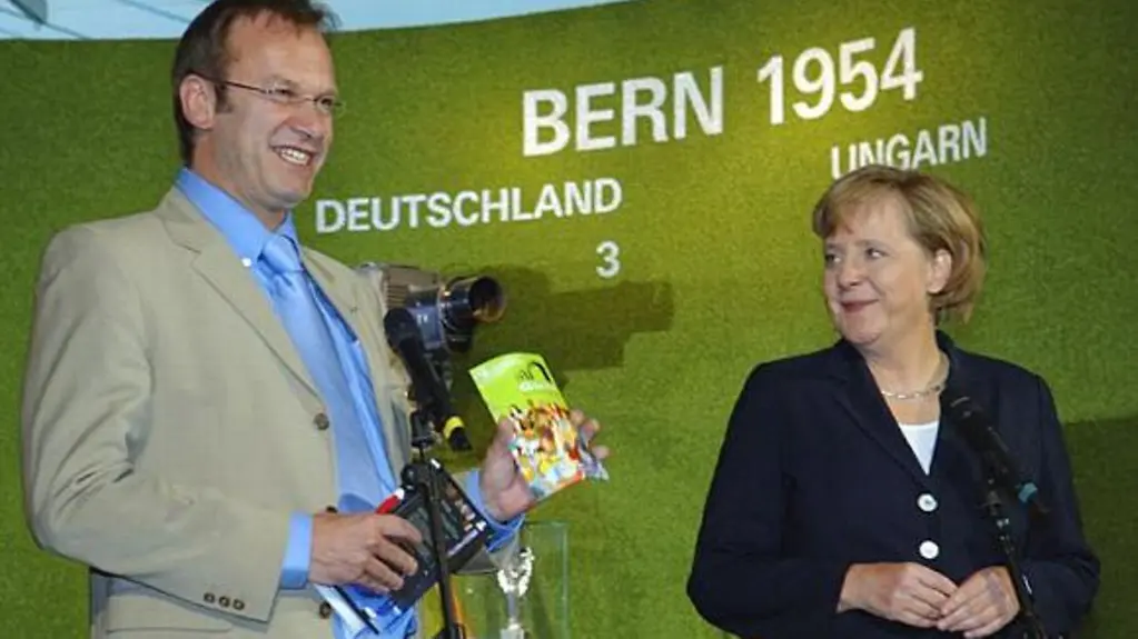La chancelière fédérale, Angela Merkel, et le directeur de la KOS, Thomas Schneider, présentent le Fanguide de la Coupe du monde de football à l'exposition sur le Mondial à la Chancellerie fédérale.