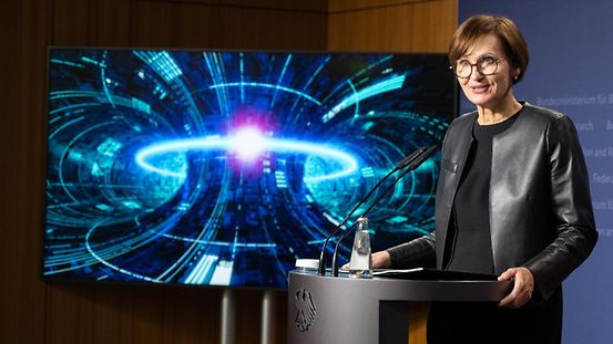Bundesforschungsministerin Stark-Watzinger am Rednerpult vor einem Symbolbild der Kernfusion.