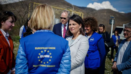 Außenministerin Annalena Baerbock spricht mit einer Frau, die eine blaue Weste der EU-Mission "EUMM Georgia" trägt. Um die beiden herum stehen weitere Personen.