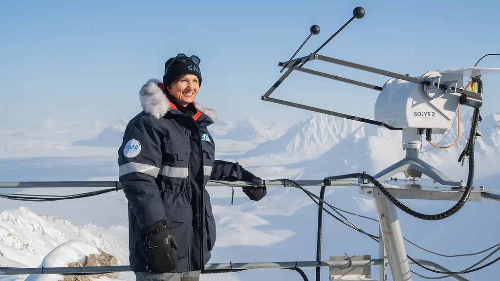 Bundesforschungsministerin Bettina Stark-Watzinger steht neben einem Forschungsinstrument. Im Hintergrund ist die Schneelandschaft von Spitzbergen zu sehen.