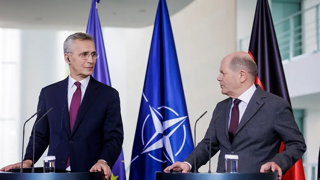NATO Secretary General Stoltenberg (left) standing at a lectern with Federal Chancellor Scholz during the press conference. In the background are three flags: EU, NATO and Germany.