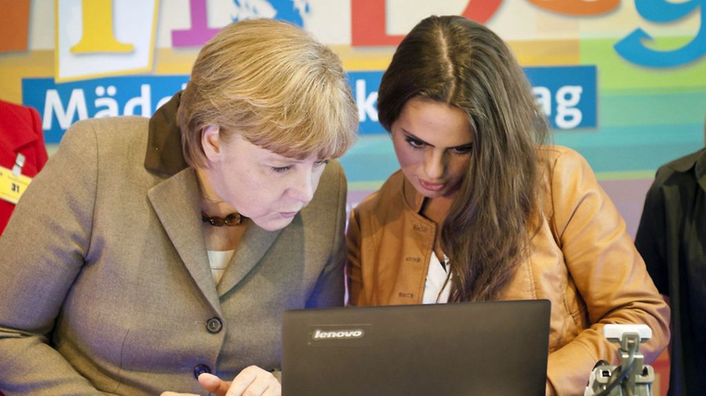 Merkel und eine Schülerin betrachten eine Girls´Day App