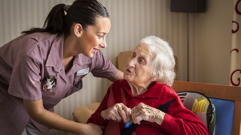 Pflegefachkraft aus Spanien hilft einer Seniorin in einer Pflegeunterkunft.