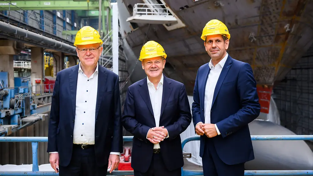 Bundeskanzler Olaf Scholz in der Mitte vor einem Schiff in der Werf. Links Ministerpräsident Stephan Weil und Minister Minister-Olaf-Lies. 
