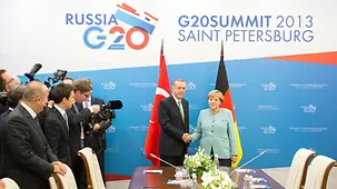 Angela Merkel and Recep Tayyip Erdogan shake hands under the summit logo.