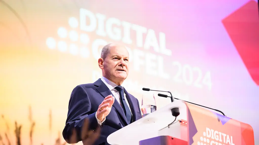Kanzer Scholz spricht am Rednerpult gestikulierende mit der rechten Hand. Im Hintergunrd das Logo der Veranstaltung "Digital gipfel 2024". 