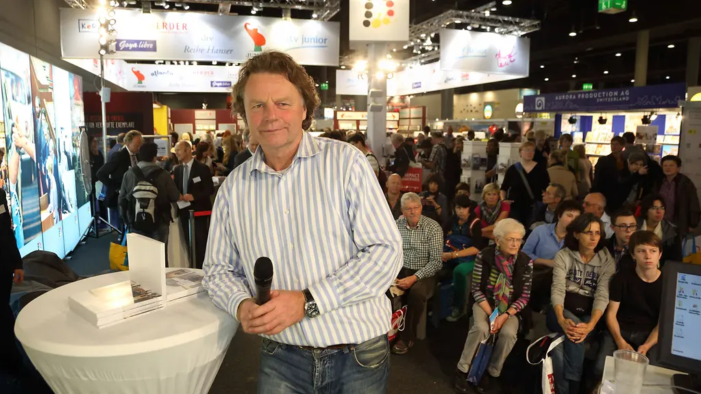 Siegbert Schefke mit Mikrofon am Stand der Bundesregierung