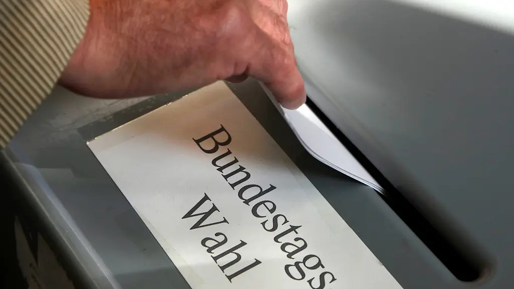 Eine Hand hält einen Umschlag und steckt ihn in einen Behälter mit einem Schlitz und der Aufschrift Bundestags-Wahl.