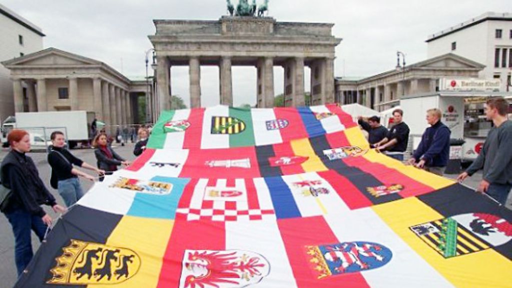 Jugendliche tragen eine große Fahne mit den Wappen der deutschen Bundesländer zum Brandenburger Tor