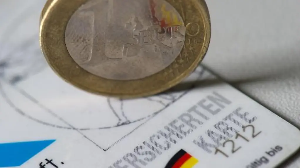 Eine Euromünze steht auf der Versichertenkarte einer gesetzlichen Krankenversicherung