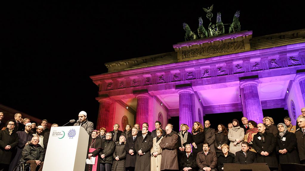 Ein Imam trägt während der Mahnwache für der Opfer der Terroranschläge von Frankreich vor dem Brandenburger Tor in Berlin Koranverse vor.