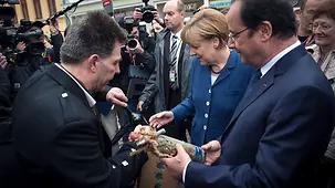 Chancellor Angela Merkel and French President François Hollande are presented with a bottle of wine.