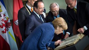 Bundeskanzlerin Angela Merkel und der französische Präsident François Hollande schauen sich eine französische Bibel aus dem 13. Jahrhundert an.