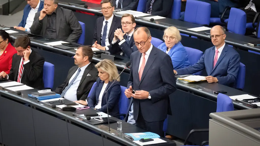 Federal Chancellor Merz stands at his place on the Federal Government bench in the Bundestag.