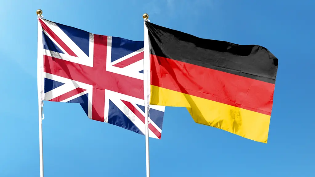 Union Jack und deutsche Flagge wehen am Himmel.