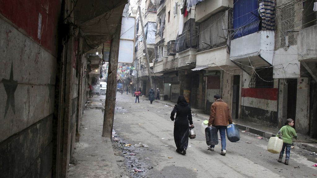 Man, woman and child carry water canisters along a stree in Aleppo
